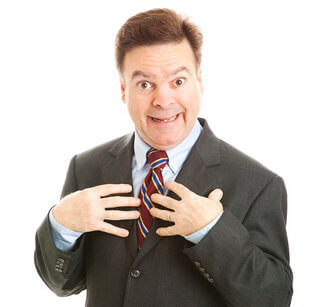 Businessman looking surprised and pointing to himself as if to say "who me?" Isolated on white.